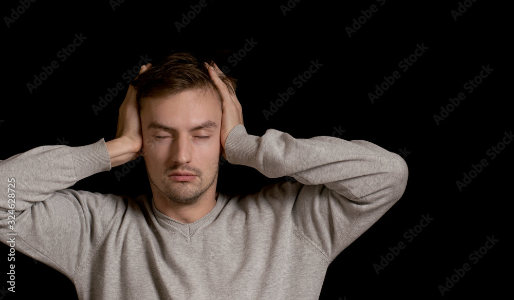 man on black background covers his ears with his hands