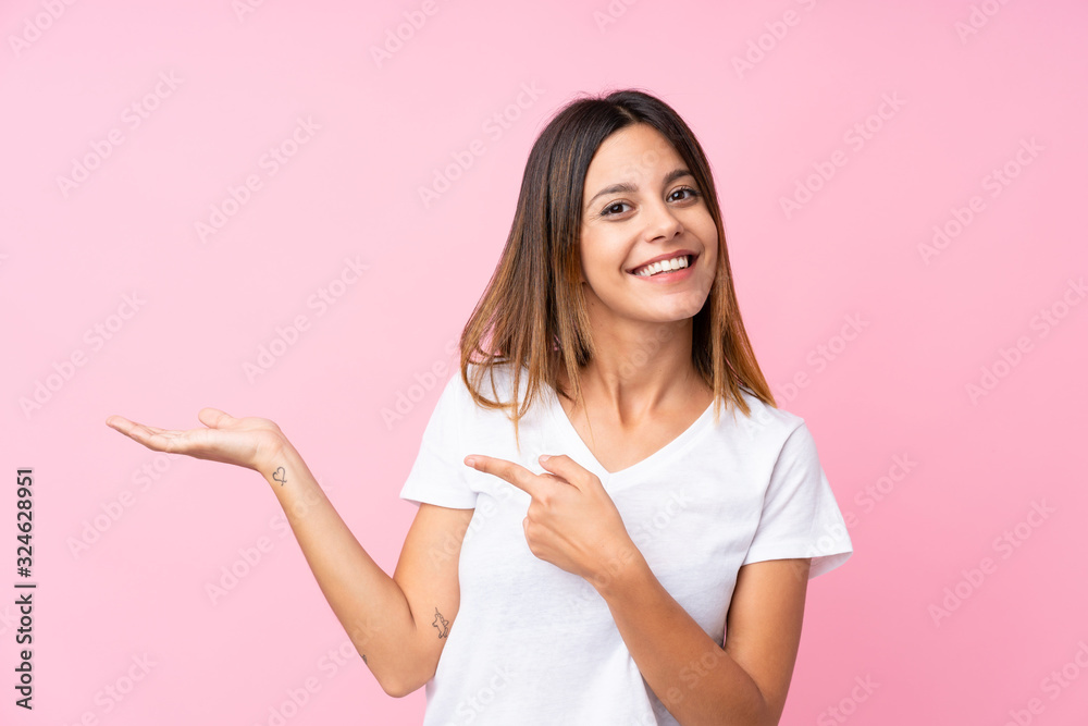 Young woman over isolated pink background holding copyspace imaginary on the palm to insert an ad