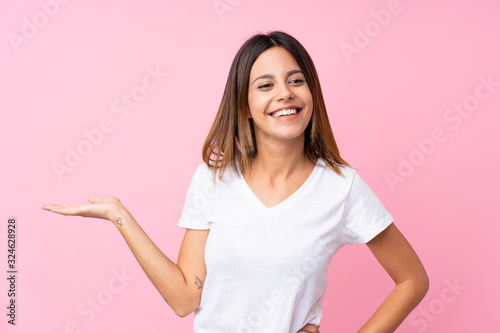 Young woman over isolated pink background holding copyspace imaginary on the palm to insert an ad © luismolinero
