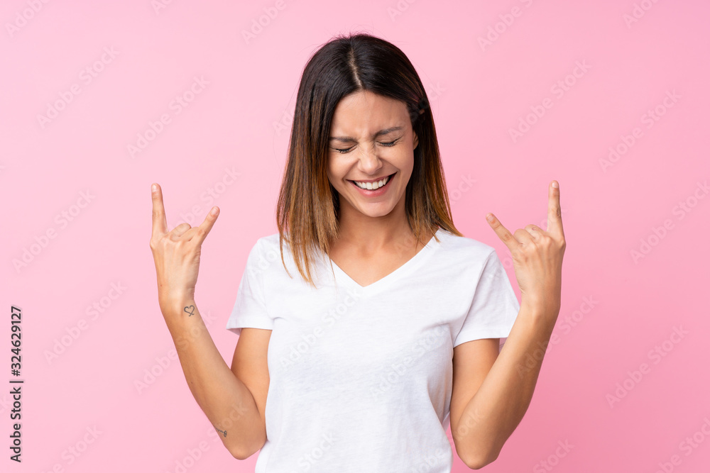 Young woman over isolated pink background making rock gesture Young woman over isolated pink background making rock gesture