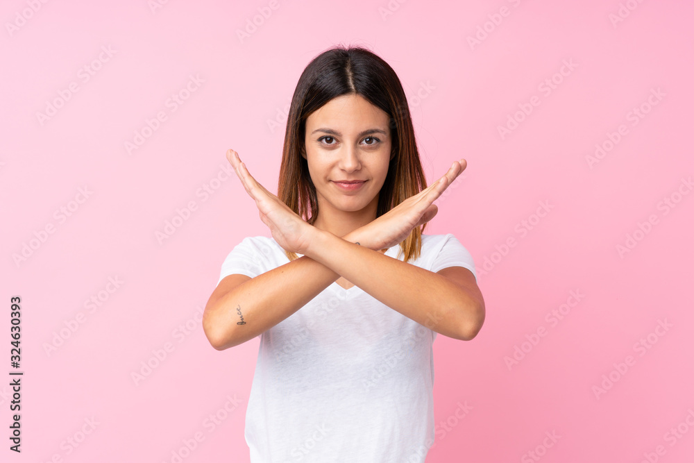 Young woman over isolated pink background making NO gesture Young woman over isolated pink background making NO gesture