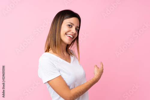 Young woman over isolated pink background pointing back