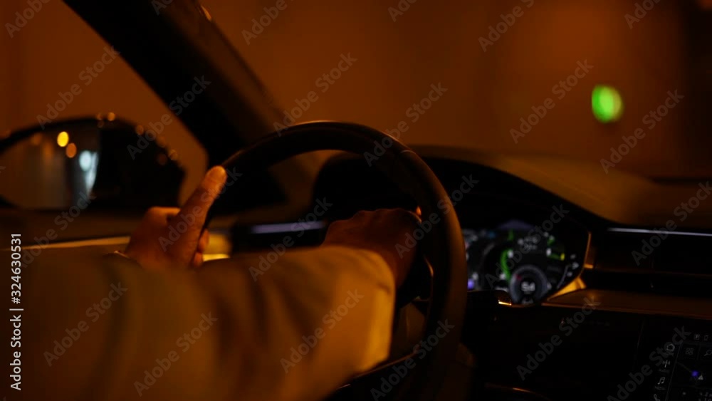 Close up view from back seat of of male hands on steering wheel in modern car driving into dark urban tunnel checking security and safety. Automobile interior with display Digital dashboard in night