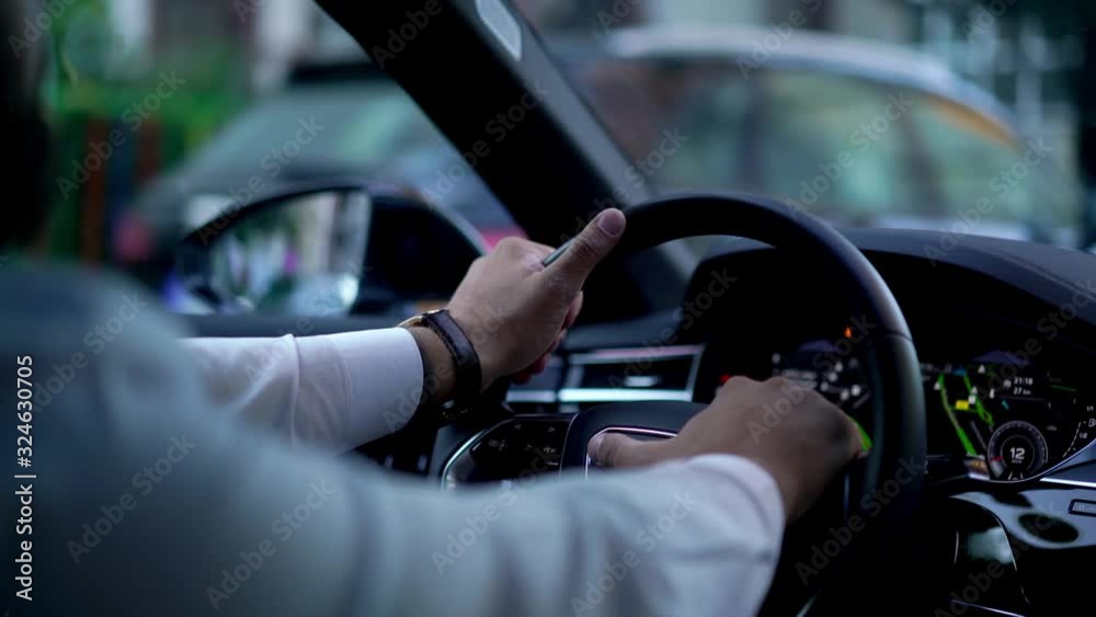 Close up view from back seat businessman in white shirt holding hands on steering wheel while driving vehicle automobile waiting for green light. Blurred city view behind windshield while car moving Close up view from back seat businessman in white shirt holding hands on steering wheel while driving vehicle automobile waiting for green light. Blurred city view behind windshield while car moving