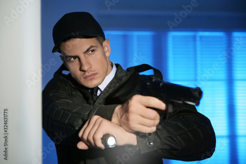Professional security guard with flashlight and gun in dark room