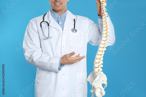 Male orthopedist with human spine model against blue background, closeup