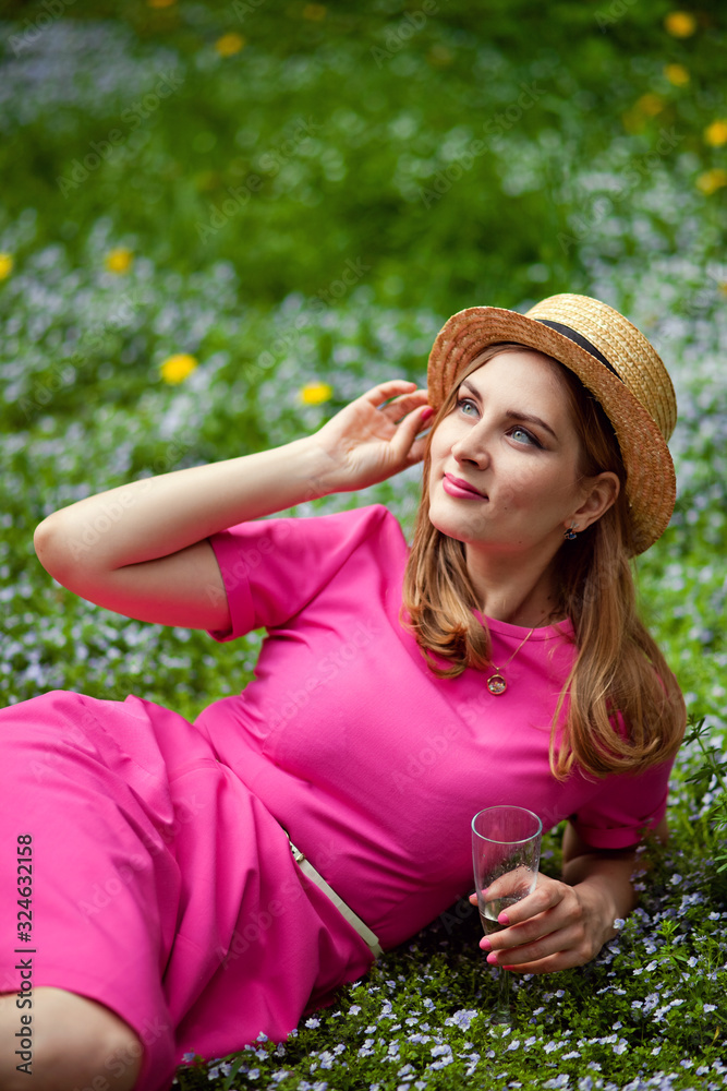 Obraz premium a girl in a blooming garden on a picnic is lying on a blanket with a glass of champagne