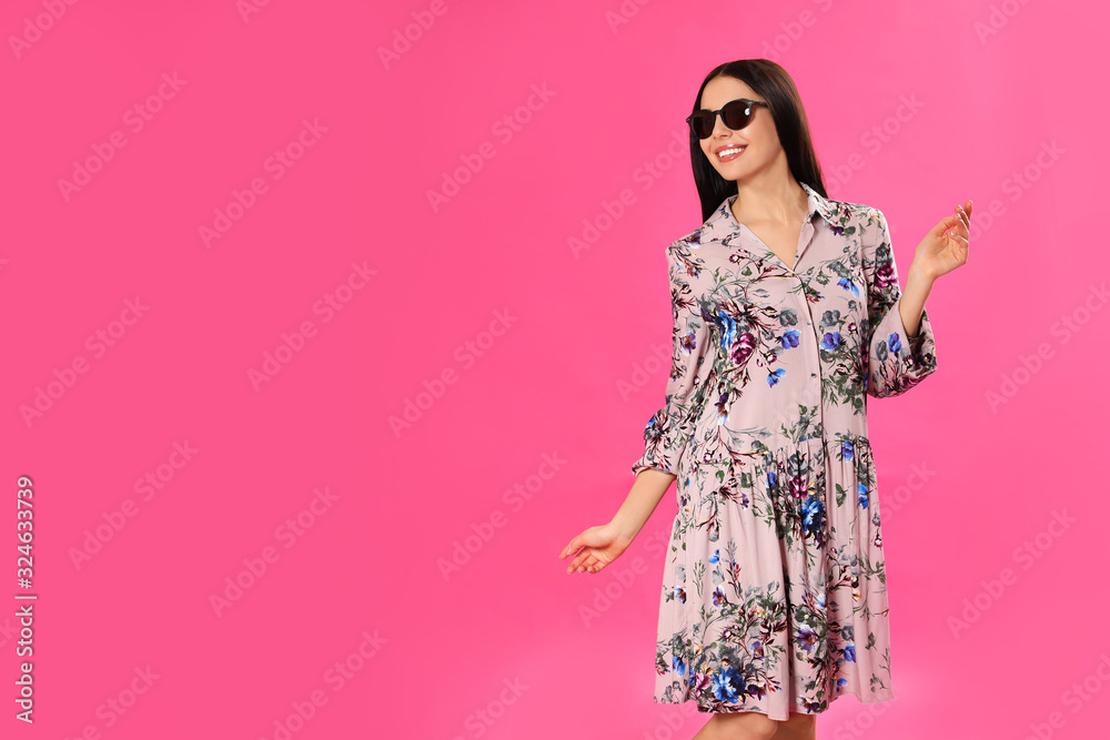 Young woman wearing floral print dress and sunglasses on pink background. Space for text