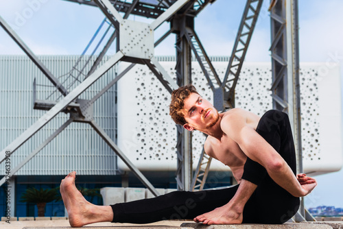 Young man in the city in the yoga position ardha matsyendrasana stretching and relaxing her body and mind.