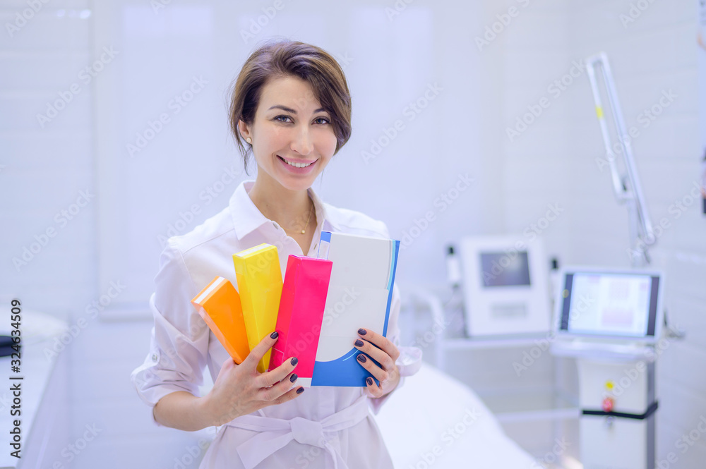 A cosmetologist dermatologist holds in his hands a package with drugs for facial rejuvenation. A female doctor in his office shows injection options. A cosmetologist dermatologist holds in his hands a package with drugs for facial rejuvenation. A female doctor in his office shows injection options.