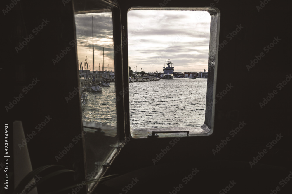 Ship moored to port seen through from inside the porthole of a ship.