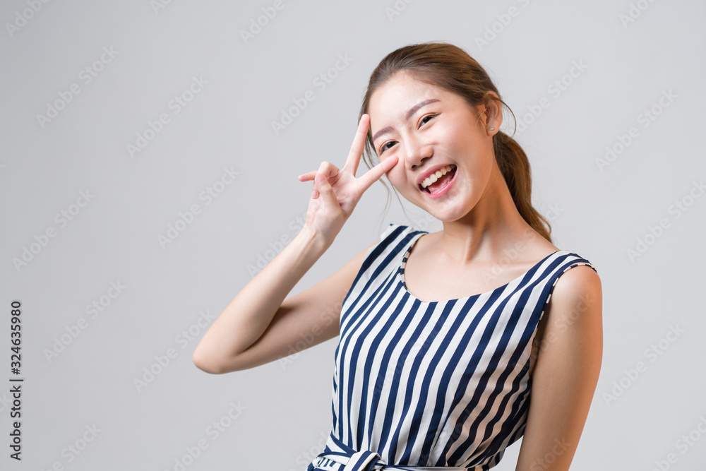 Young Asian woman smiling and raising her hand like victory or winner, feeling successful and happiness life on grey background.