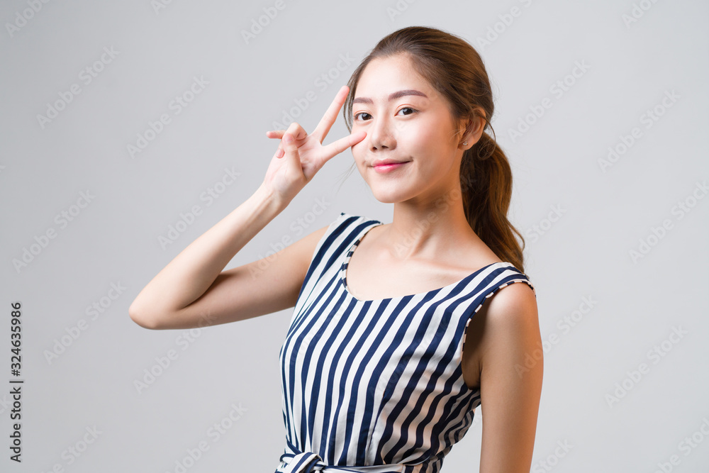 Young Asian woman smiling and raising her hand like victory or winner, feeling successful and happiness life on grey background. Young Asian woman smiling and raising her hand like victory or winner, feeling successful and happiness life on grey background.