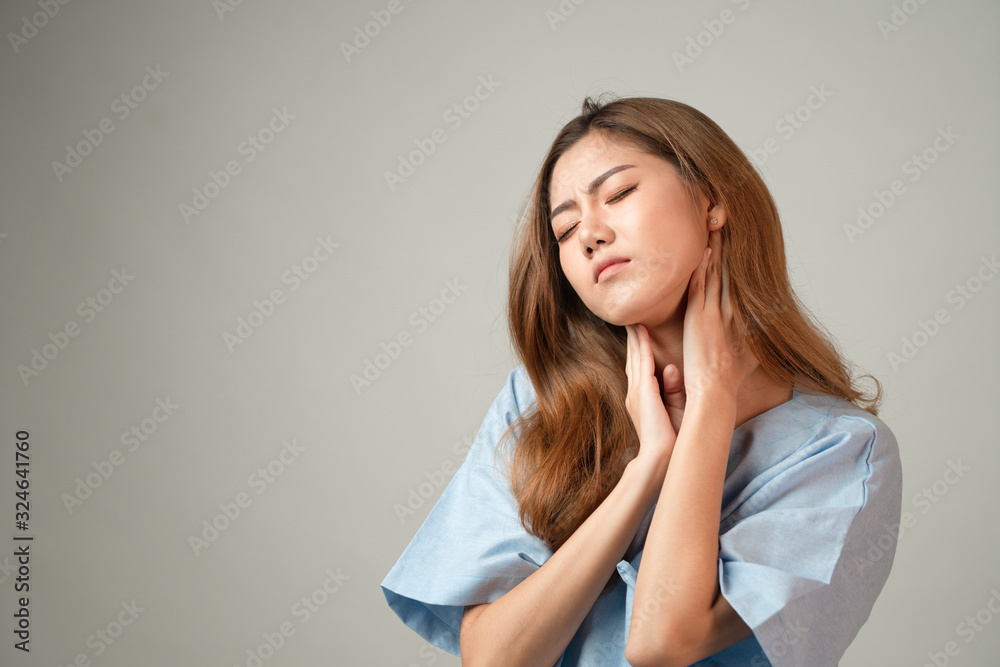 Portrait of a beautiful Asian woman in patient gown raised her hands and touch her neck feeling like pain from office syndrome on gray background with copy space, concept healthcare insurance. Portrait of a beautiful Asian woman in patient gown raised her hands and touch her neck feeling like pain from office syndrome on gray background with copy space, concept healthcare insurance.