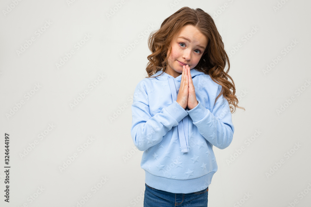cute teenage girl in a blue hoodie prays to buy something on a light gray background cute teenage girl in a blue hoodie prays to buy something on a light gray background