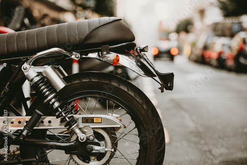 Close-up of vintage motorcycle rear wheel and leather seat parked on urban street with blurred red brake lights