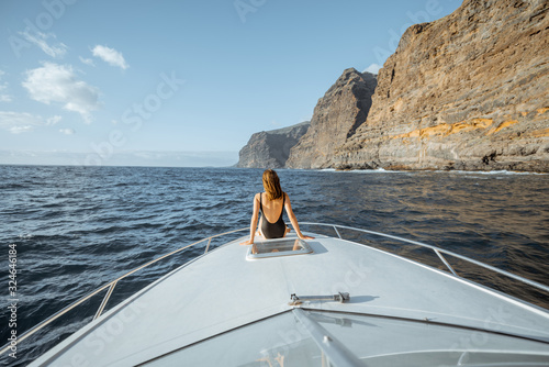 Woman enjoying ocean voyage sitting back on the yacht nose while sailing near the breathtaking rocky coast on a sunset. Wide seascape view photo