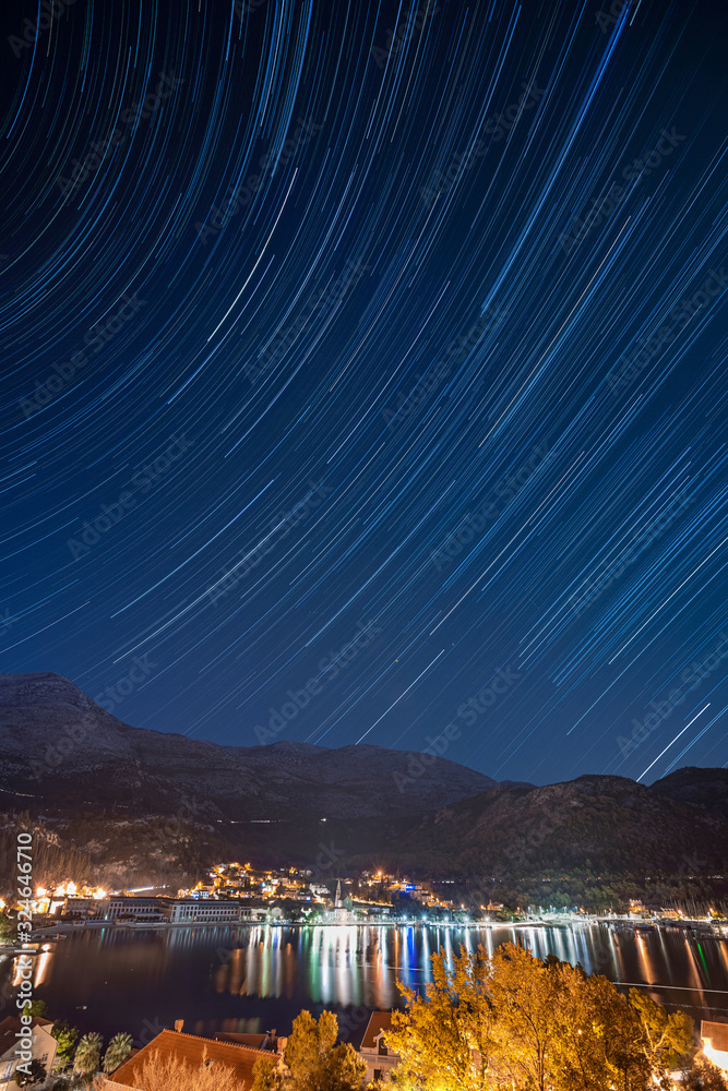 Landscape of a night town on beachfront with star trails on a deep blue sky, long exposure