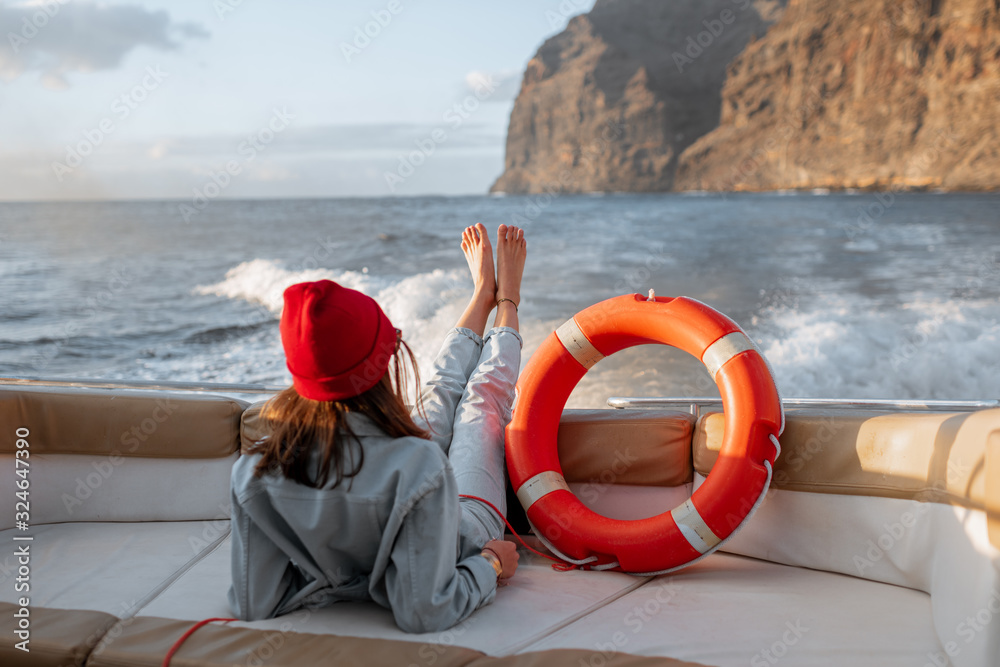 Young woman with lifebuoy enjoying sea voyage, sailing on a yacht near a rocky shore. Concept of a carefree lifestyle and travel