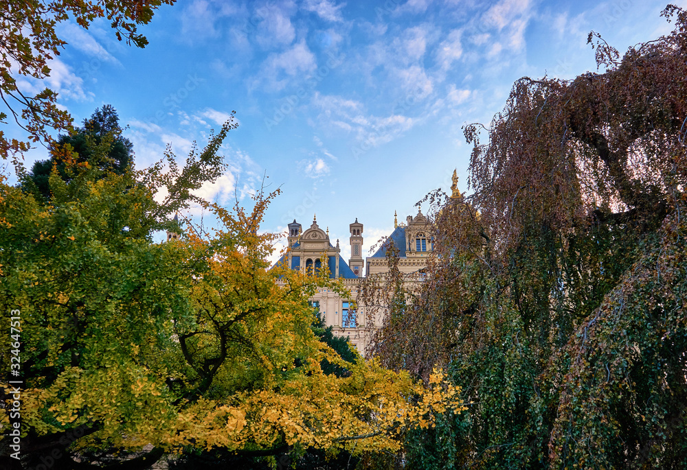View of the Schwerin Castle through the trees in the castle garden. With blue sky and clouds in the background.