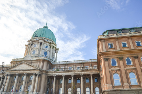 Buda Castle in Budapest, Hungary with light blue sky and clouds above. Historical castle and palace complex of the Hungarian kings. Facade with pillars, balconies and cupola. Tourist attraction © ppohudka