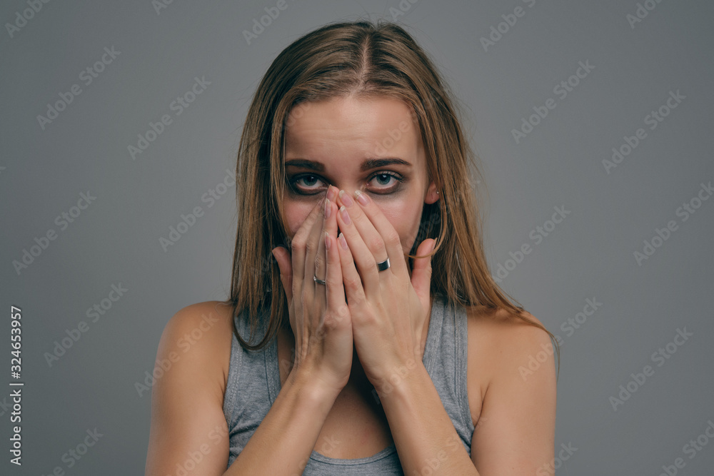 Blonde girl with bruises covering her face posing against gray background. Domestic violence, abuse. Depression, despair. Close-up, copy space.