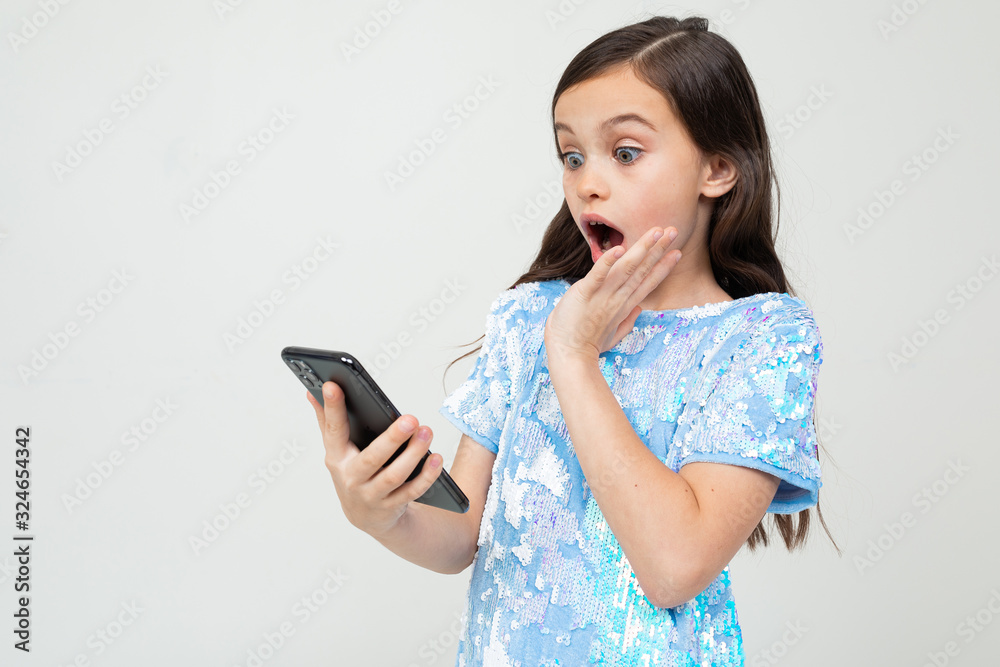 surprised teenager girl emotionally looks at the phone on a white studio background surprised teenager girl emotionally looks at the phone on a white studio background