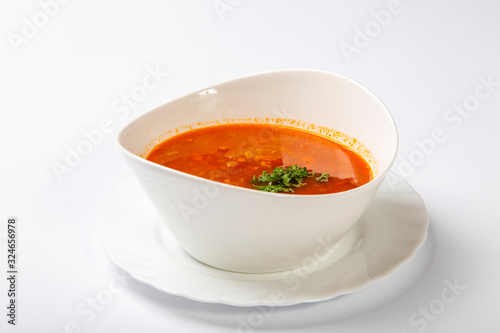 Beef goulash soup with tongue. A white oval plate with red soup stands on a white background