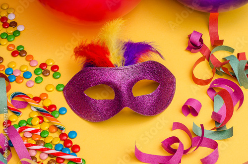 Carnival. Festive background with copy space. Carnival mask purple with feathers on a yellow background with tinsel, multi-colored sweets. Mardi Gras. Brazilian.