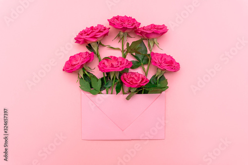 Holiday concept. Bouquet of pink roses in pink envelope on pink background. Mock up, flat lay, top view, copy space. Wedding invitation cards or love letter. Valentine's day or other holiday concept © Veronika