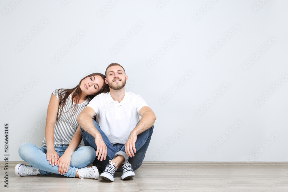 Happy young couple sitting on the floor on grey background