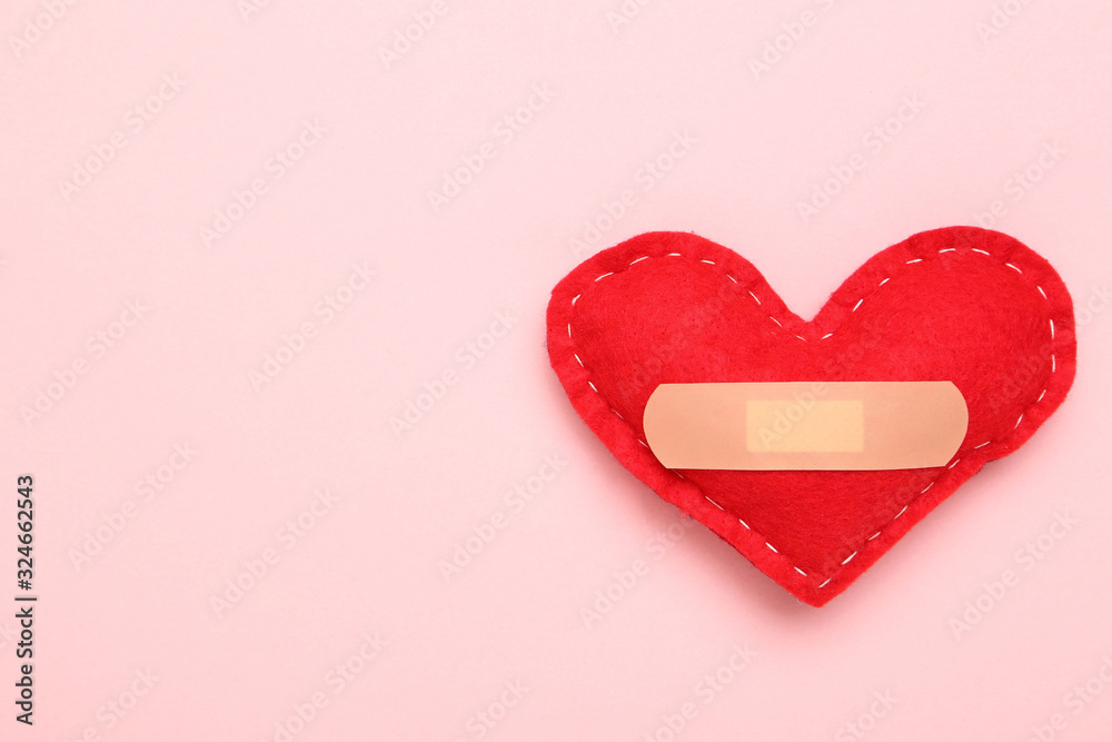 Red fabric heart with bandage on pink background