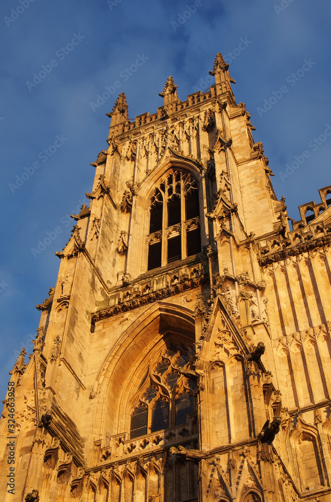 Fototapeta premium side view of one of the towers at the front of york minster in sunlight against a blue cloudy sky