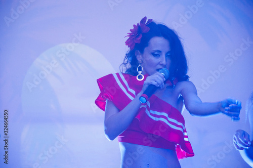 Latin hot singer. Hispanic woman with microphone. Havana style girl, woman with red flower in hair. Spanish music evening. The singer on stage. Stage light. Dia de los Muertos. Argentina dance