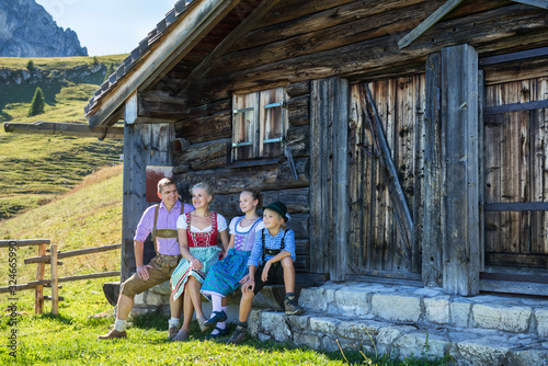 Young Bavarian family in a beautiful mountain landscape. Happy parents and smiling kids in traditional Bavarian clothes at an old hut