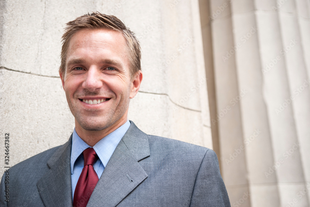 Candid portrait of smiling businessman looking at the camera outdoors with copy space on traditional columns Candid portrait of smiling businessman looking at the camera outdoors with copy space on traditional columns
