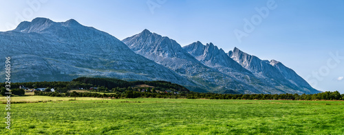 Panoramic view at five of Seven Sisters Mountain range on Sandnessjoen, ideally green grass, small Norwegian village and mountains beside the field. Shinny sunny day, blue skies, Norway, copy space photo