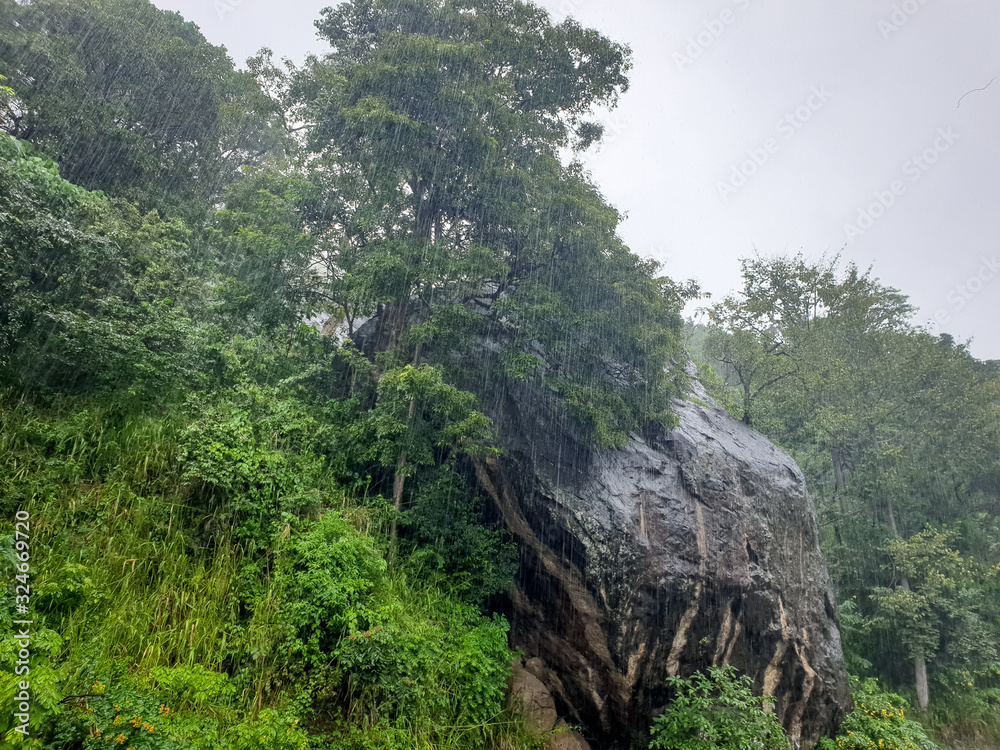 Beautiful landscape of tropical rain over the big rock and jungle forest in mountains