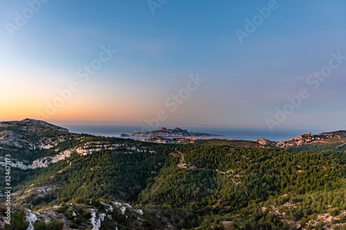 Sunrise at Calanque de Morgiou (Marseille, France): the breathtaking view of the cliff mountain landscape and the island Riou in the distance under the warm soft sunlight