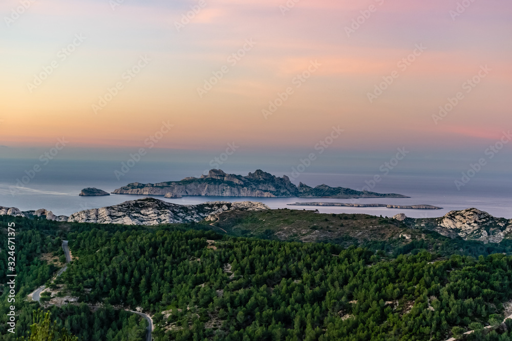 Sunrise at Calanque de Morgiou (Marseille, France): the breathtaking view of the cliff mountain landscape and the island Riou in the distance under the warm soft sunlight