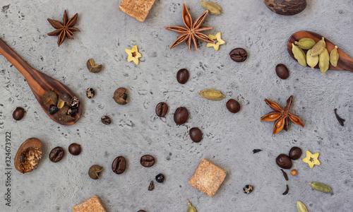 Ingredients for making spicy Indian masala chai tea or coffee: dry anise star seeds, cardamom, black pepper and brown sugar on grey stone background.