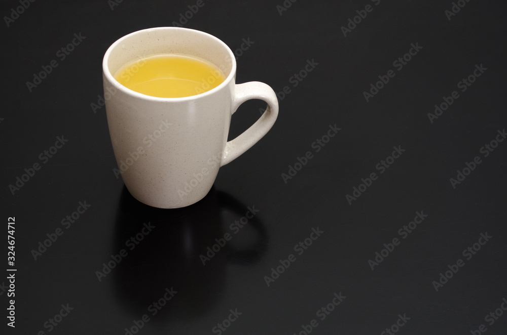 White cup on a black smooth table with reflection, with a yellow tea inside, near a brick wall with copyspace White cup on a black smooth table with reflection, with a yellow tea inside, near a brick wall with copyspace