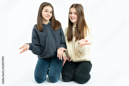 Indignant young girls in casual clothes crouched, looking at the camera and shrugging, isolated over white background