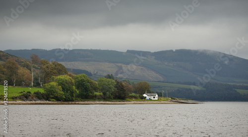 Panoramic view of the rocky shores of Kyles of Bute from the water. Hills and mountains in the background. Cows graze in the valley.. Dark storm sky. Bute island, Firth of Clyde, Scotland, UK photo