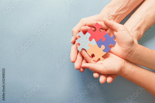 Adult and chiild hands holding jigsaw puzzle shape, Autism awareness, Autism spectrum family support concept, World Autism Awareness Day