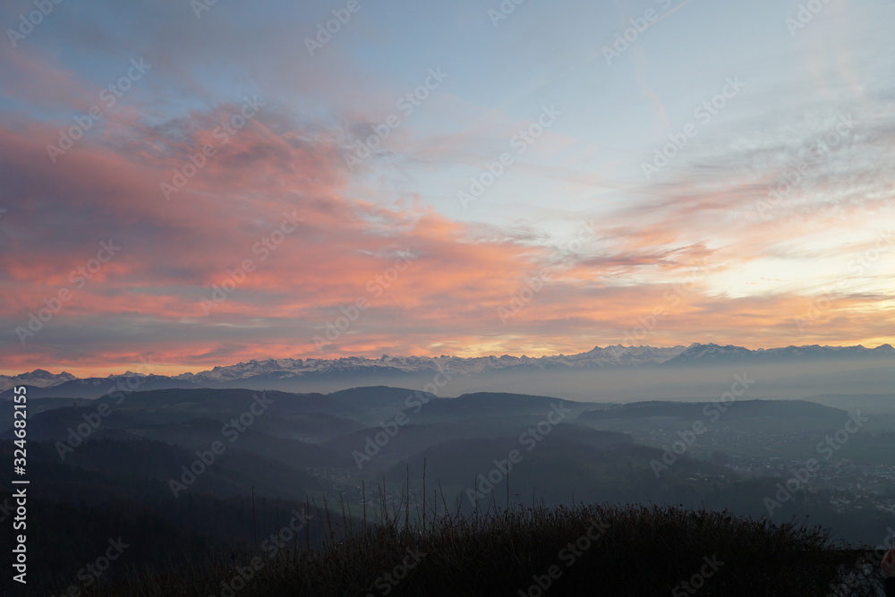 Sunset panorama of Alps over canton Zurich, Switzerland. The whole landscape is veiled in thin fog. The sky is partially colorful at sunset. 