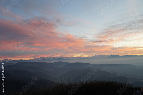 Sunset panorama of Alps over canton Zurich, Switzerland. The whole landscape is veiled in thin fog. The sky is partially colorful at sunset.  © Lucia