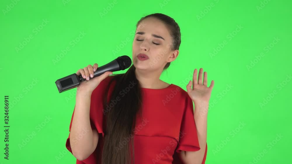 Portrait of pretty young woman is singing into a microphone and moving to the beat of music. Green screen Portrait of pretty young woman is singing into a microphone and moving to the beat of music. Green screen