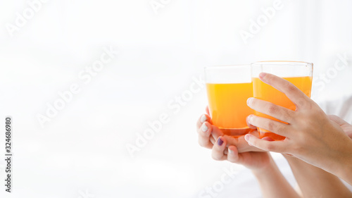Close up women's hand hold glass of orange juice on bright background with copy space on left side.