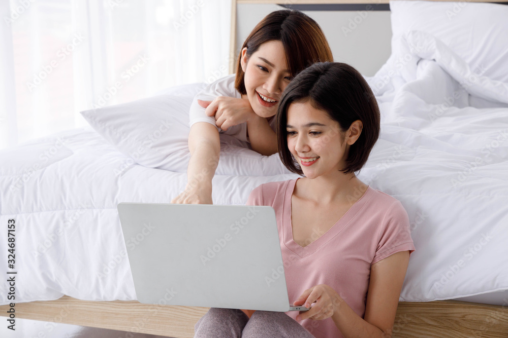 Two Happy Asian women smile and look at laptop in bright bedroom. Concept for teenage or friends activity, lifestyle at home. Two Happy Asian women smile and look at laptop in bright bedroom. Concept for teenage or friends activity, lifestyle at home.